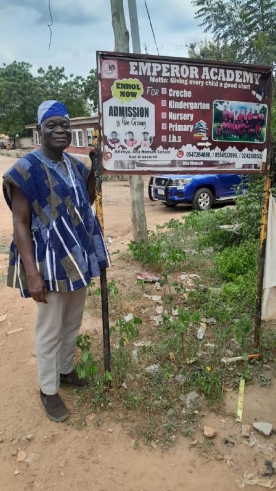 Ministry founder standing beside the Emperor Academy signboard in Afienya